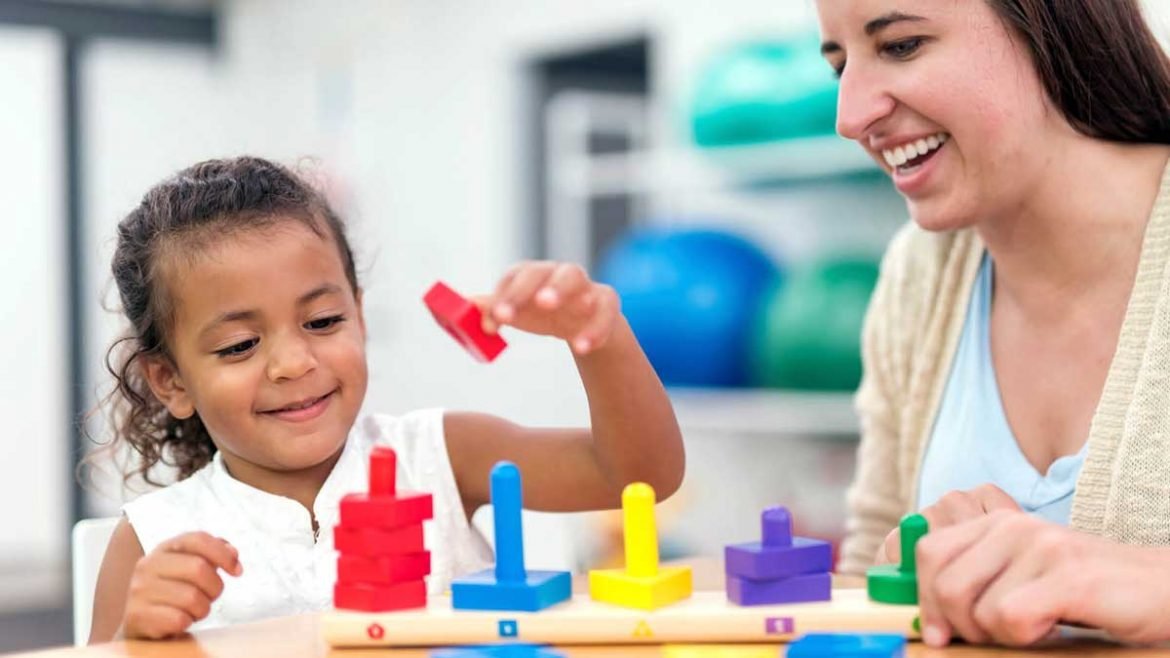 Occupational therapist working with a young girl on fine motor skills and hand-eye coordination using colorful stacking pegs