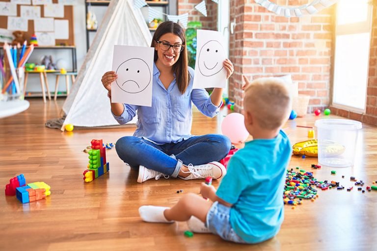 Child behavioral therapist using visual emotion cards to teach feelings recognition and social skills to a young boy during a play therapy session.