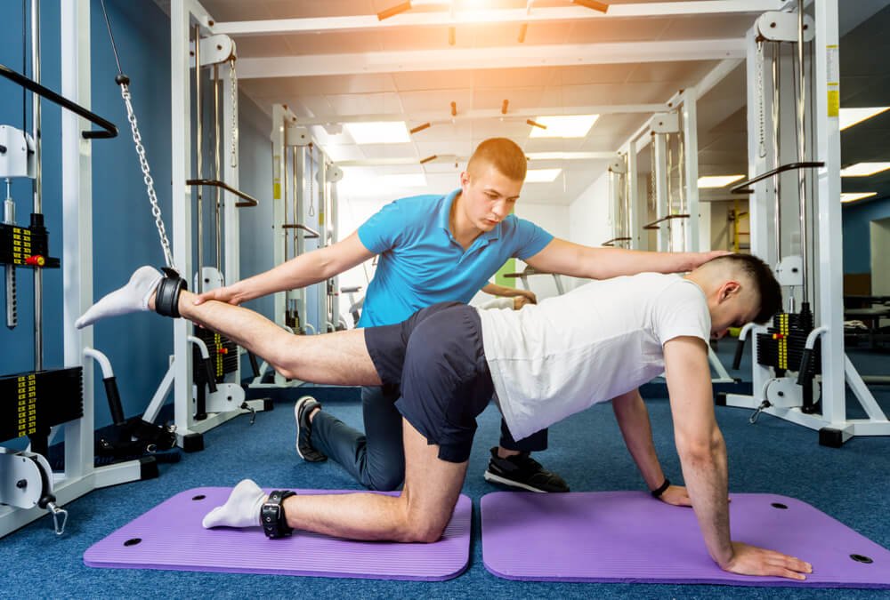 Physiotherapist guiding a patient through weighted hip extension exercises using a cable machine for lower body strengthening.